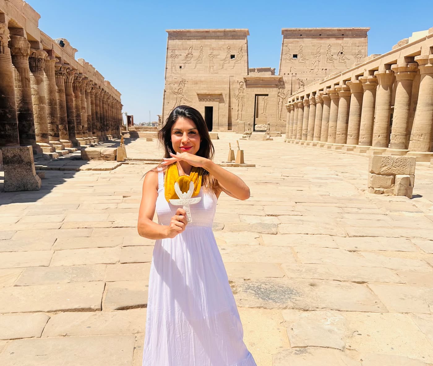 Cyntìa Assis sorrindo no Templo de Ísis, em Philae, Egito, segurando um ankh dourado